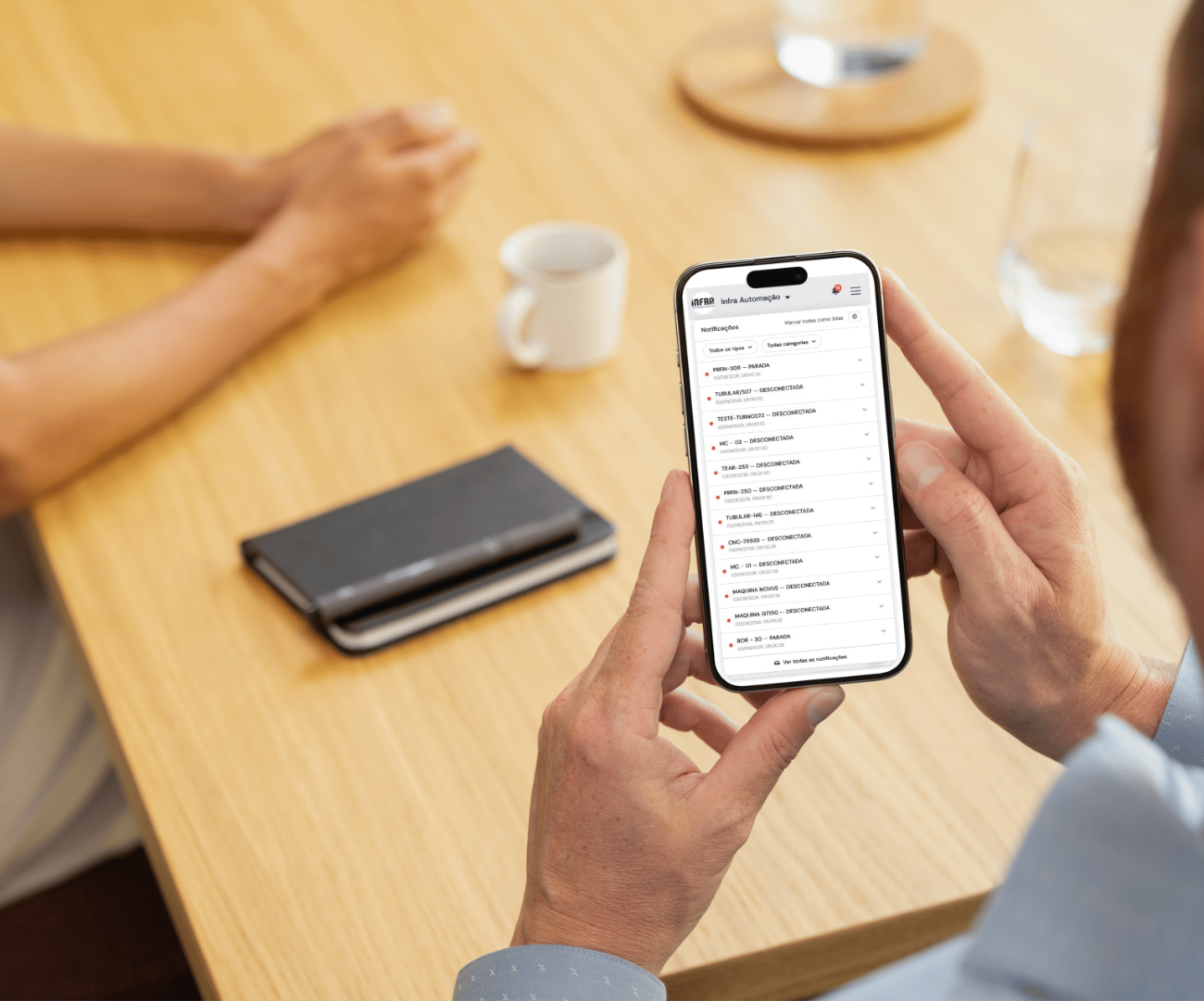Pessoa segurando um smartphone exibindo notificações de alertas de máquinas, como parada e desconexão